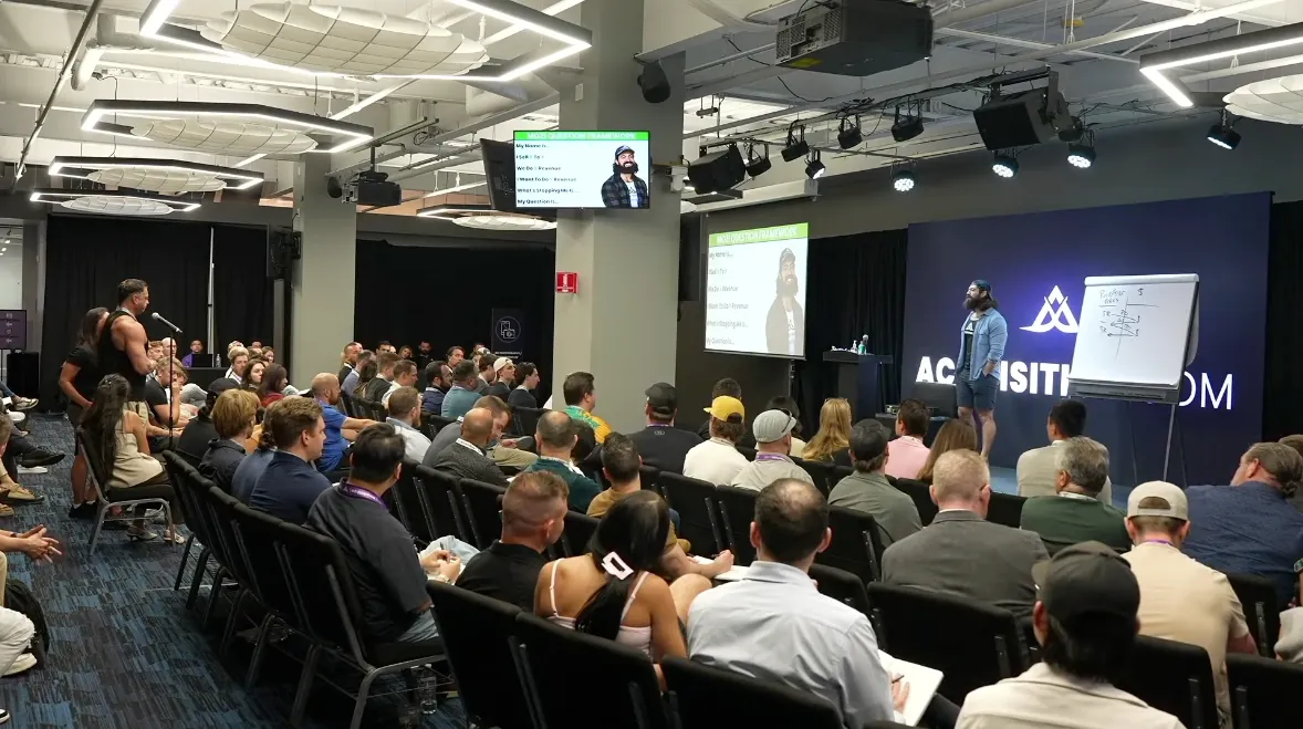 Alex Hormozi on stage taking questions from business owners at Acquisition.com