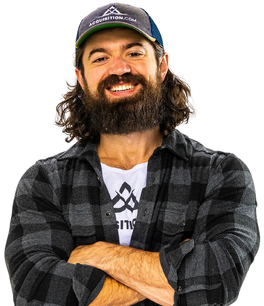 Alex Hormozi in an Acquisition.com cap and black plaid shirt, smiling with his arms folded